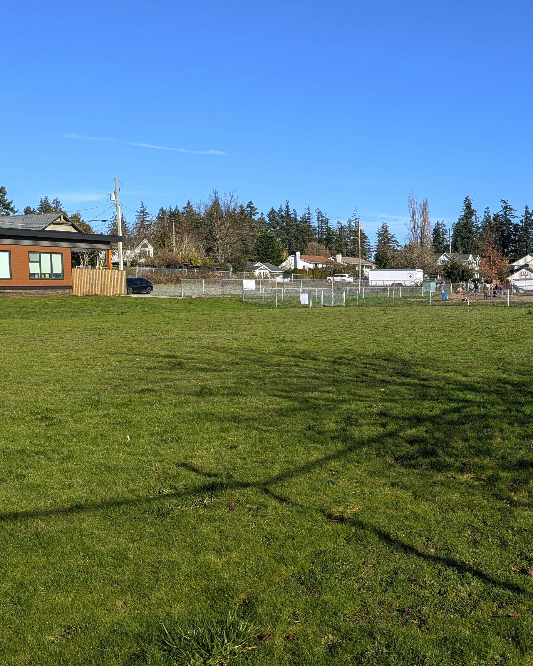 green grassy field with fanced dog park in distance